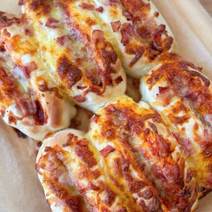 Three baked bread rolls topped with melted cheese and diced ham, placed on a parchment-lined surface.